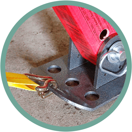 A yellow tow strap is hooked into a mounted steel base with a red bracket and a secure latch, resting on a concrete surface.